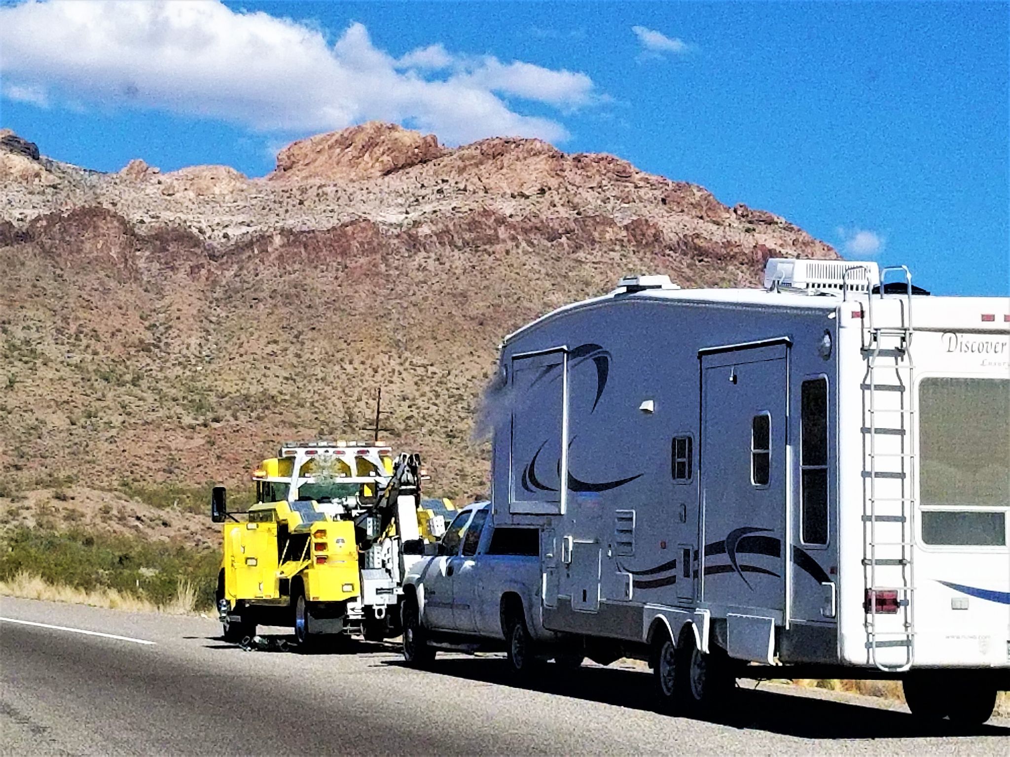 a white truck and a yellow truck on the side of a road
