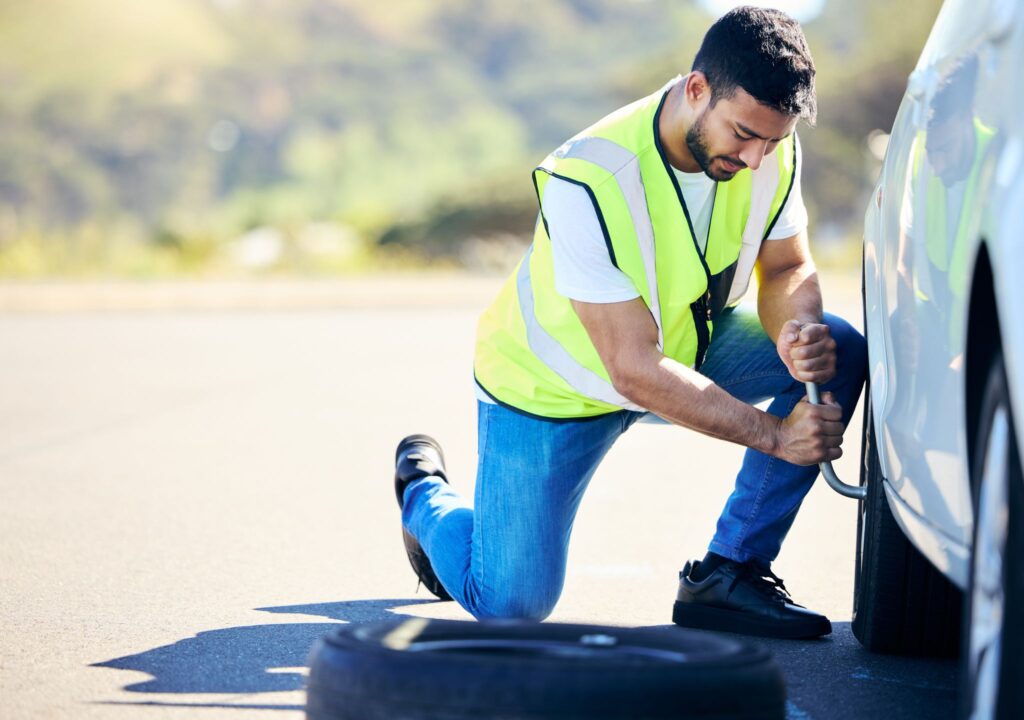 Shot of a young man changing a flat tyre on his car in a rural area.